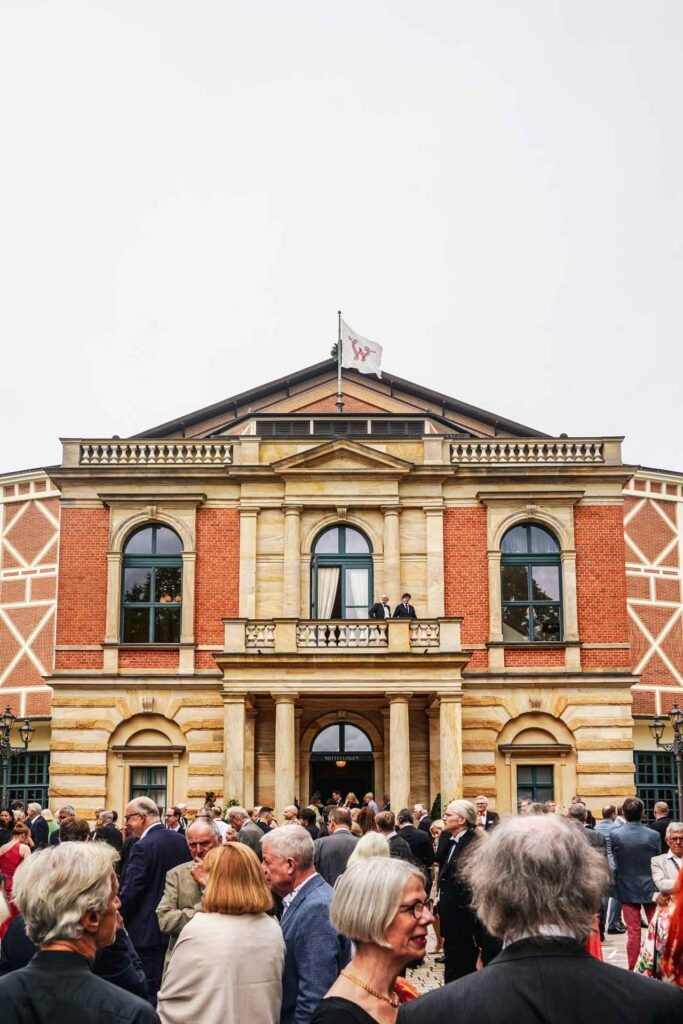 Mit Geldermann bei den Bayreuther Festspielen 2025: Das Publikum vor dem Haupteingang des Bayreuther Festspielhauses wartet auf die Pausenmusiker auf dem Balkon, die den nächsten Akt ankündigen