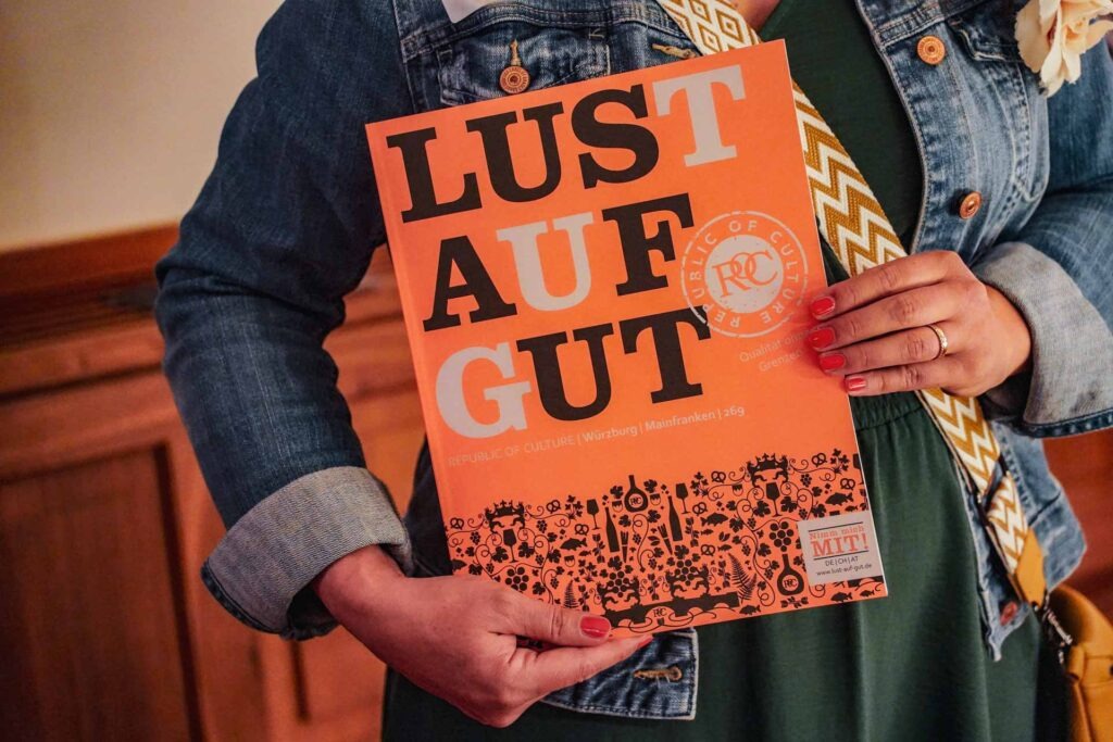 LUST AUF GUT Würzburg-Mainfranken Magazin, Ausgabe Frühjahr 2026. Alexandra von Tables and Fables hält das Magazin bei der Preview auf Schloss Castell in den Händen